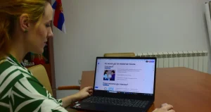 Žena sedi za stolom i posmatra sadržaj na ekranu laptopa.