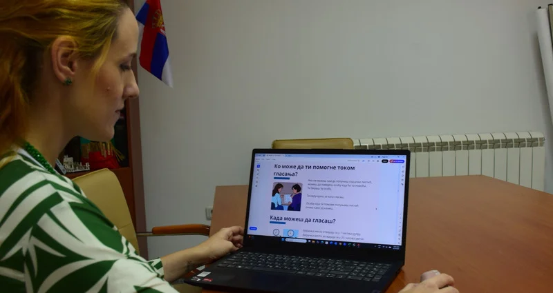 Žena sedi za stolom i posmatra sadržaj na ekranu laptopa.