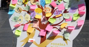 Instalacija NURDOR-a u obliku drveta, prekrivena raznobojnim porukama podrške, sa natpisom „Podrška zlata vredna“.